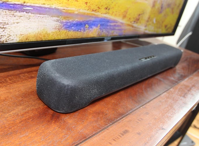 A side view of a gray Yamaha soundbar on a wooden TV stand.