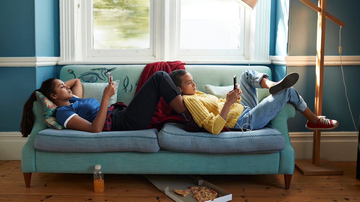 Two women sitting on the couch together, both holding smartphones.