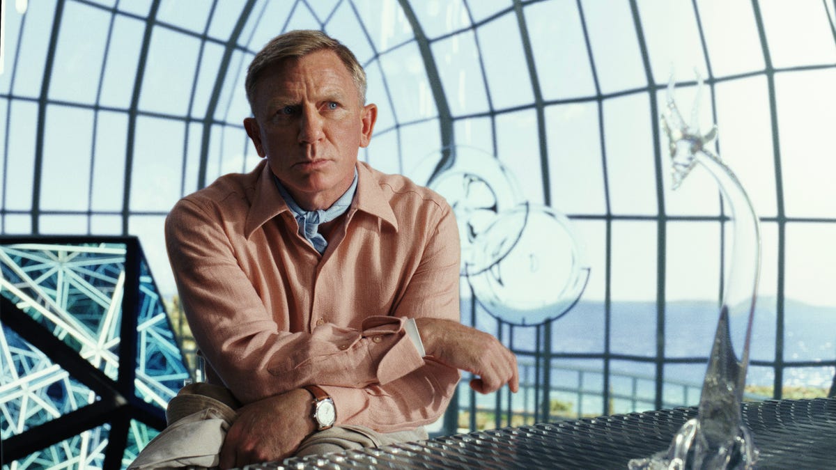 Daniel Craig looks thoughtful in a light pink shirt and blue neckerchief in murder mystery movie Glass Onion.
