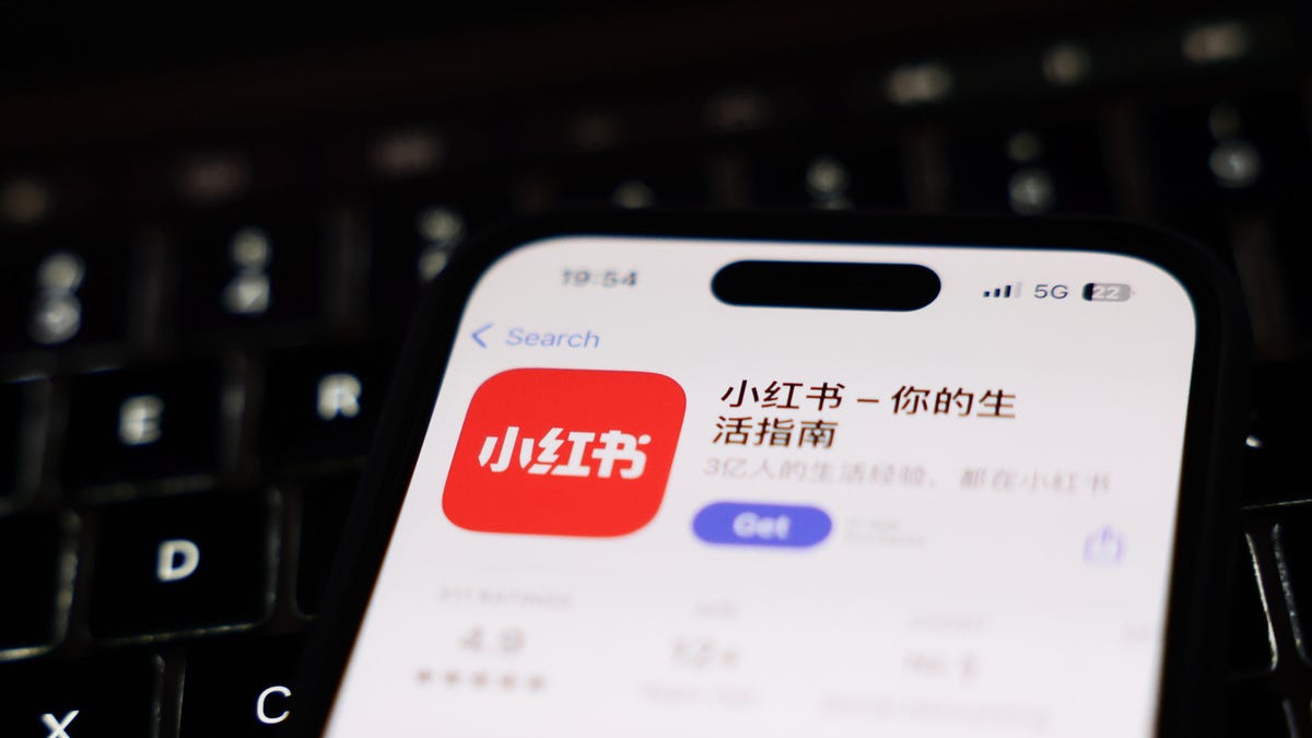 the Chinese language app Xiaohongshu is shown on a smartphone hovering over a black computer keyboard