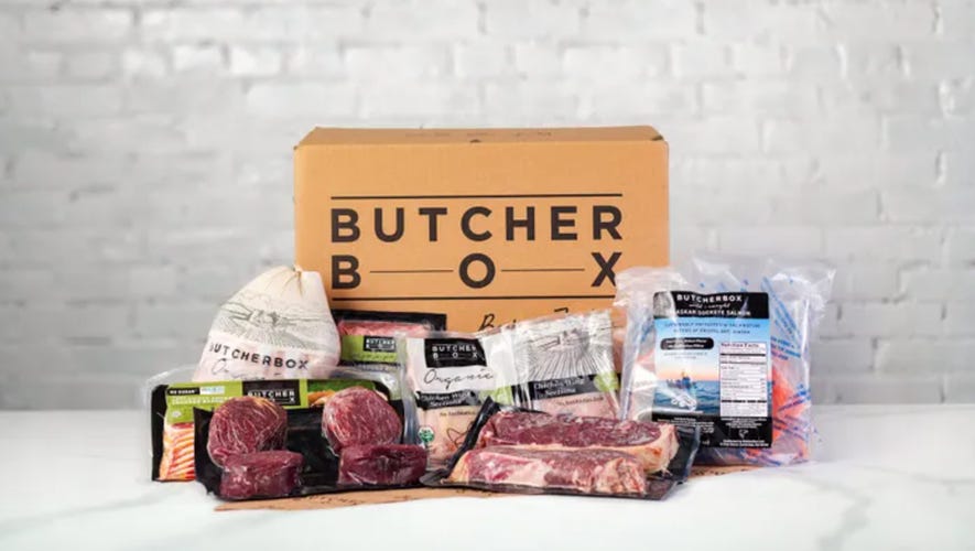 A collection of packaged meats in front of a cardboard box with the ButcherBox logo.