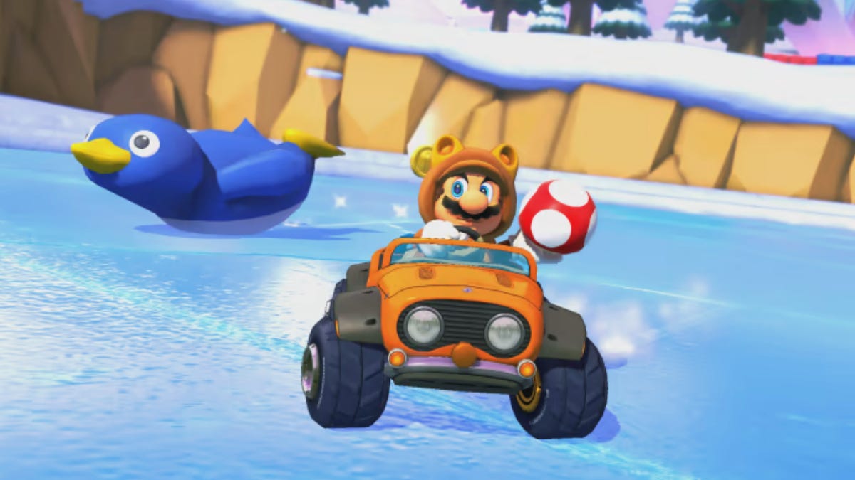 Tanooki Mario prepares to use a mushroom as penguin slides behind him on Mario Kart 8's Snow Land track
