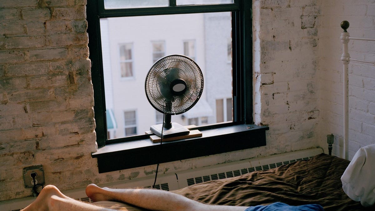 A man lying on a bed with a fan blowing