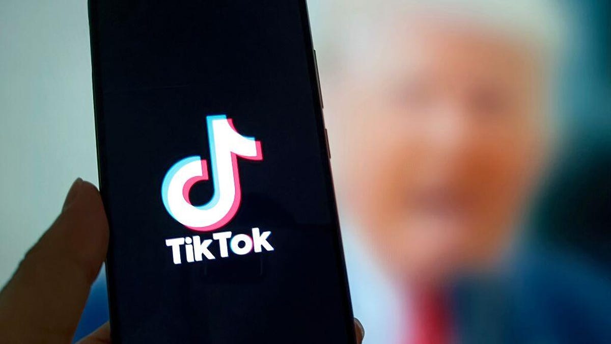 TikTok logo on a mobile phone, with a blurry image of Donald Trump in the background