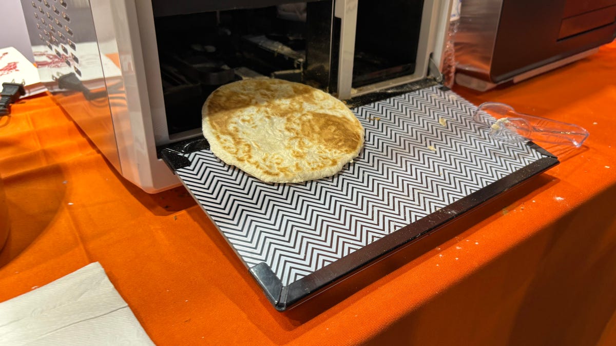 A brown tortilla slides out of a sliver machine onto a tray.