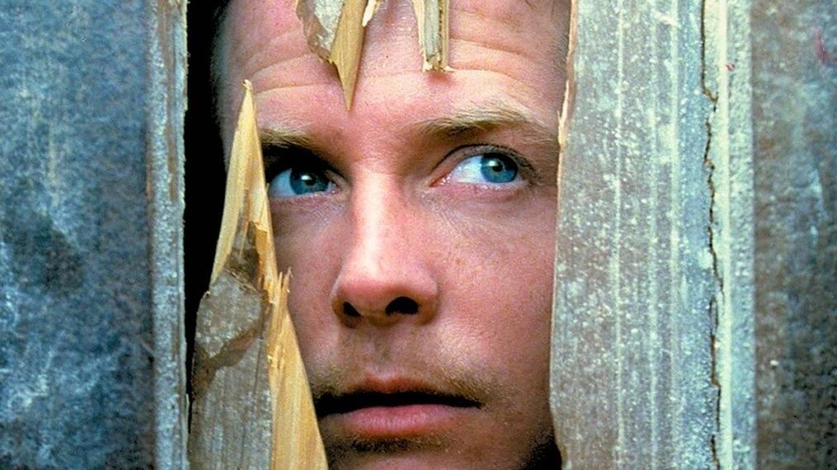 in a still from the movie The Frighteners, actor Michael J. Fox stares wistfully through a crack in a door that has been split open