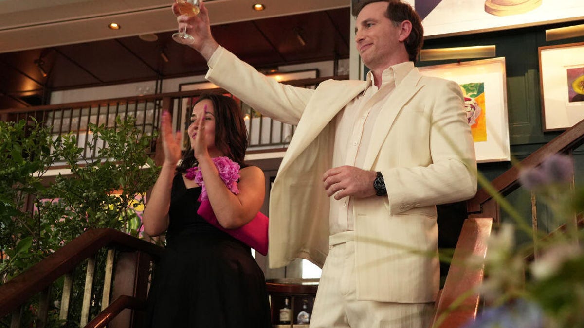 Joe Gebbia, dressed in a cream-colored suit, raises a glass of wine in a toasting gesture.