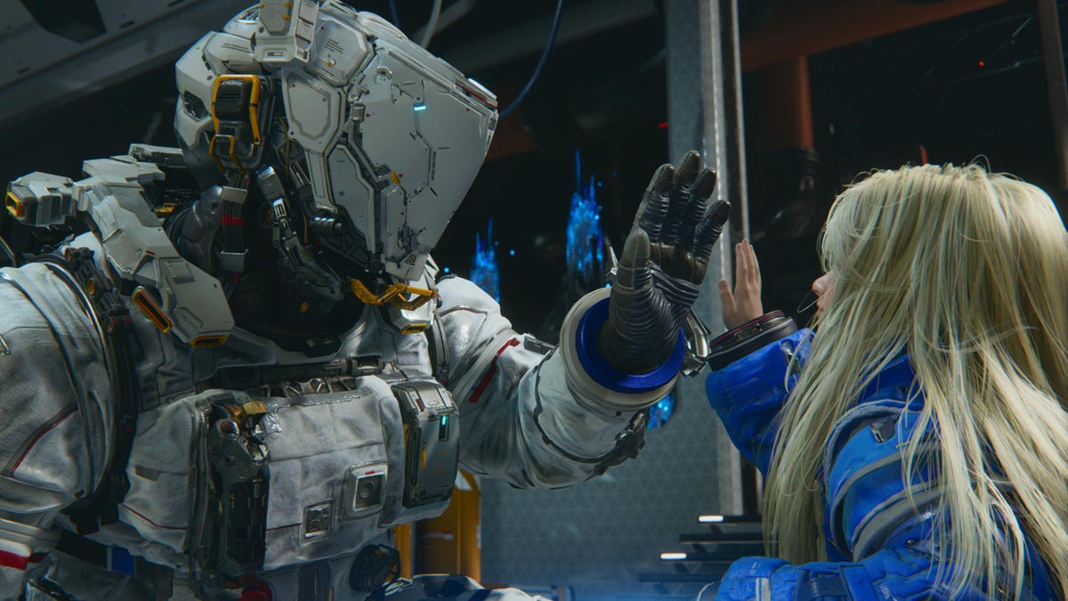 A man in a space suit holds up his hand for a high-five with a blonde girl android.