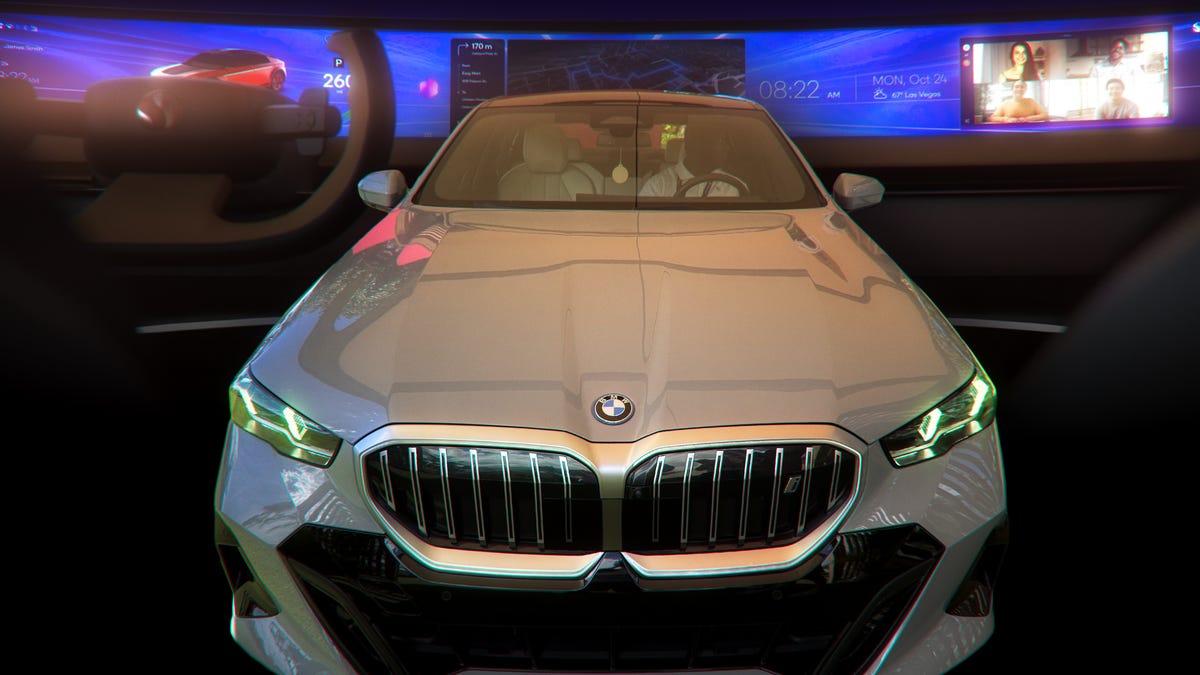 Front view of a gray BMW i5 against a backdrop of an ultrawide dashboard screen