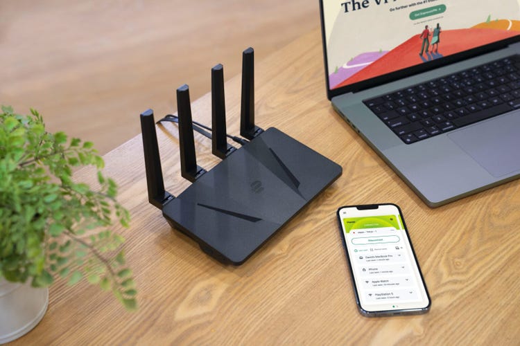 A compact router with 4 antennas rising vertically out of its back side. The router is low in profile, similar to that of a nearby cellphone and MacBook