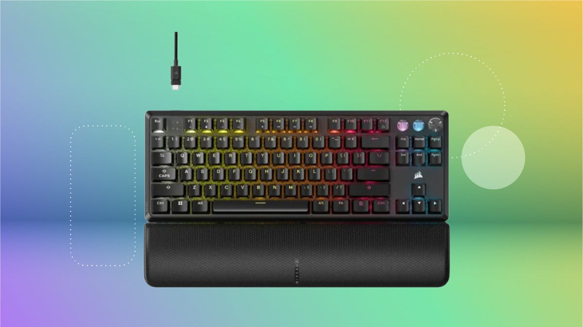 Black gaming keyboard with wrist pad and backlights on a purple, blue, green and yellow gradient background.