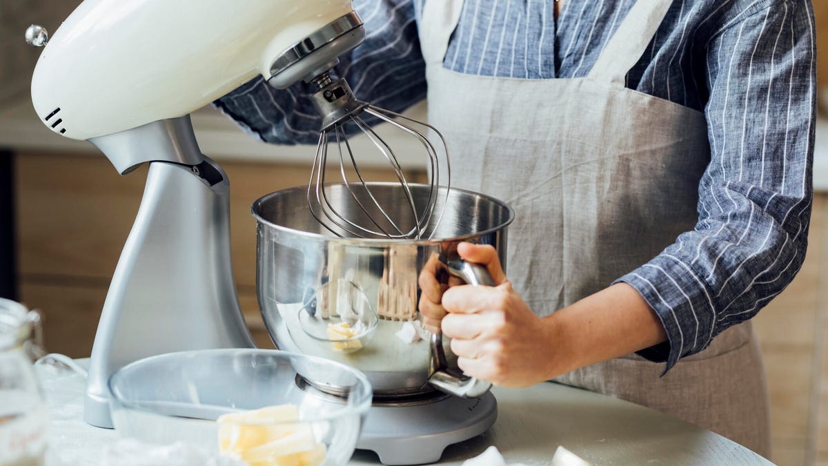 Hands of a woman in an apron using a stand mixer at home.