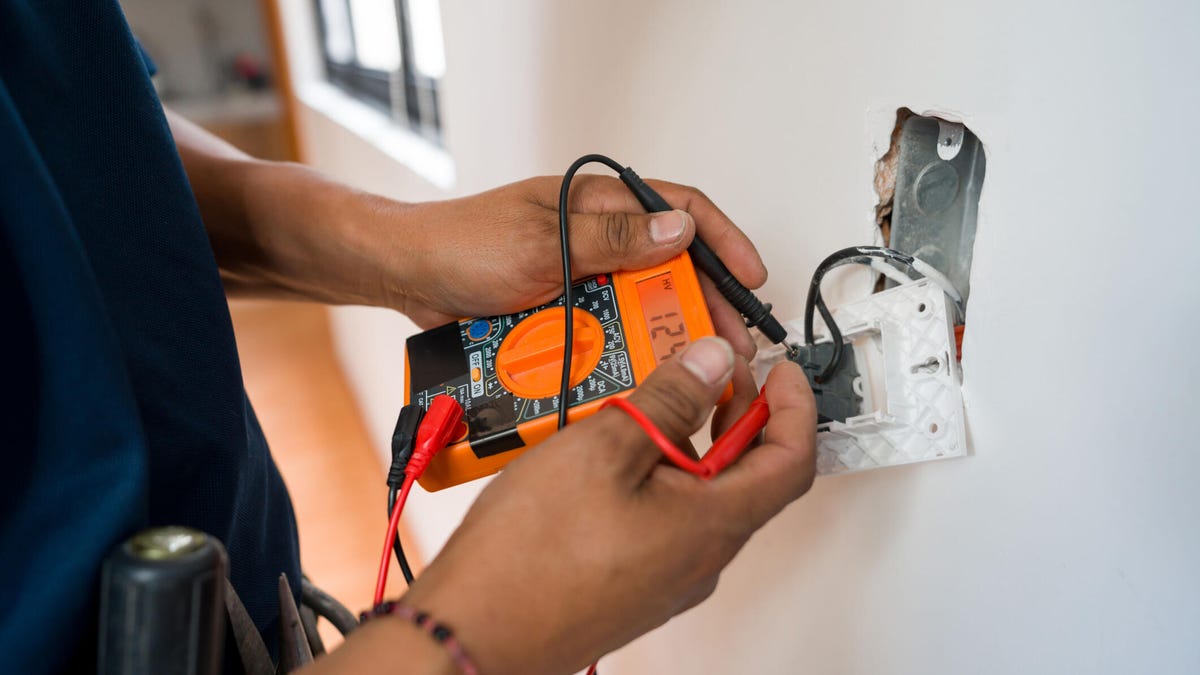An electrician measures voltage at a wall outlet they are fixing.