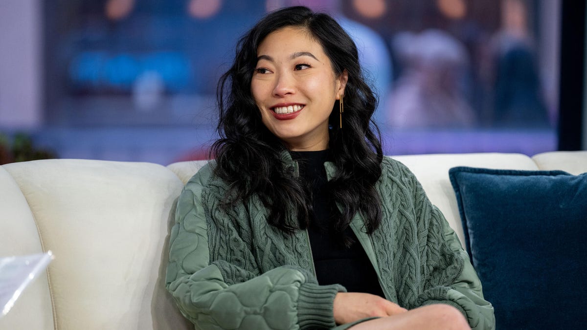Awkwafina smiling as she sits on a sofa and looks toward her interviewer, who's out of the frame.