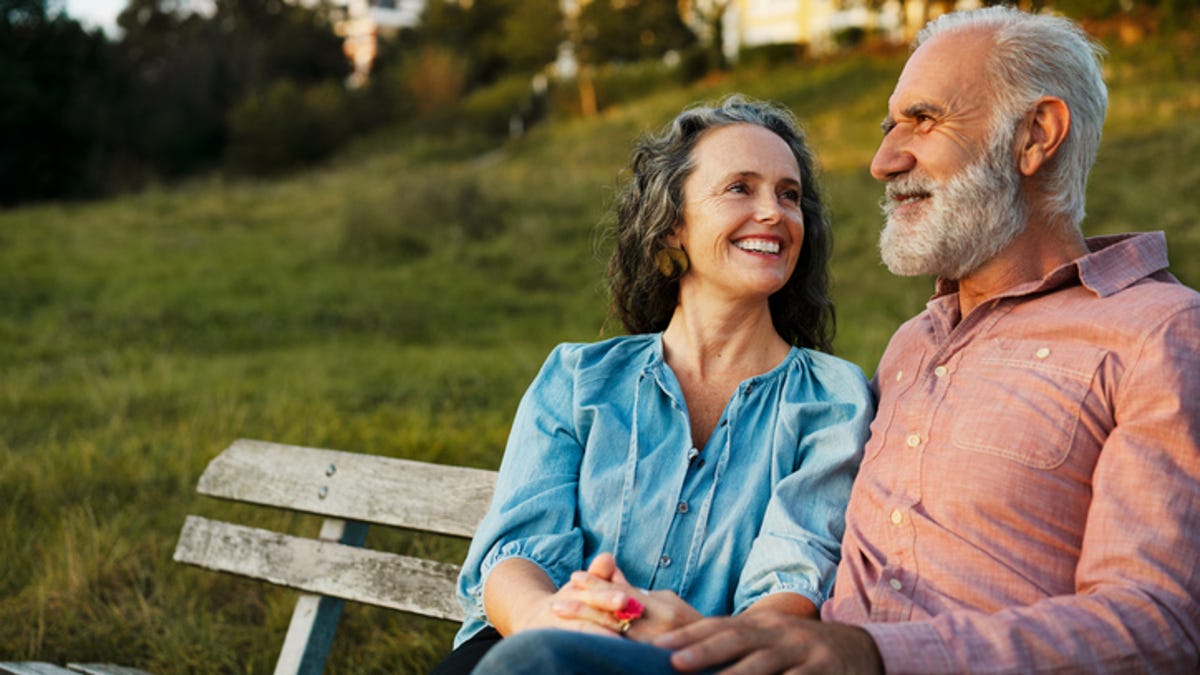 A man and a woman talking while sitting on a bench in the park.