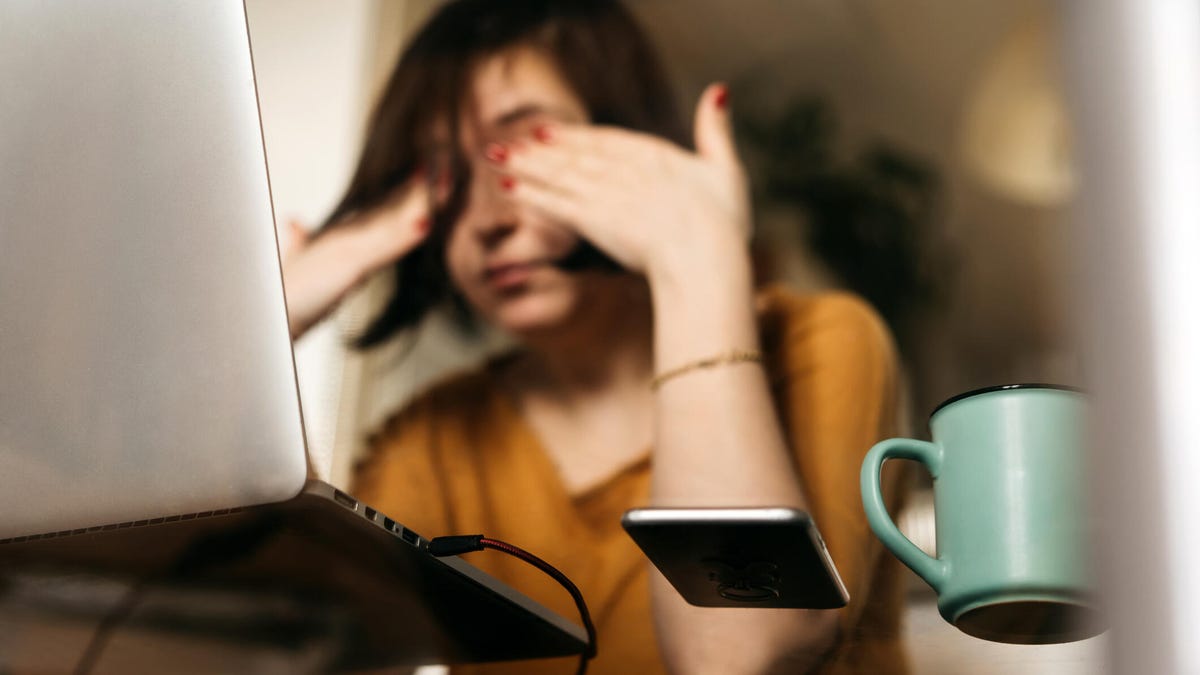 a woman sitting at her desk in front of a computer with coffee, rubbing her eyes