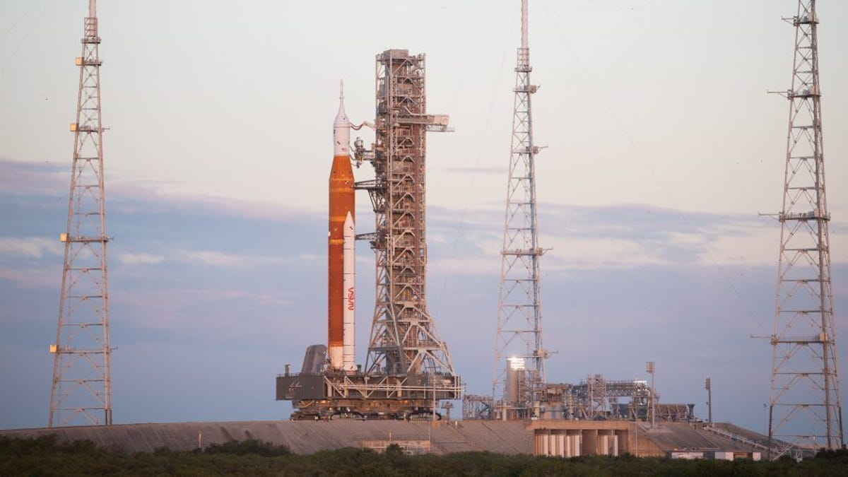 Massive SLS rocket with Orion capsule on top is atop a crawler-transporter arriving at Florida launchpad on a cloudy morning.