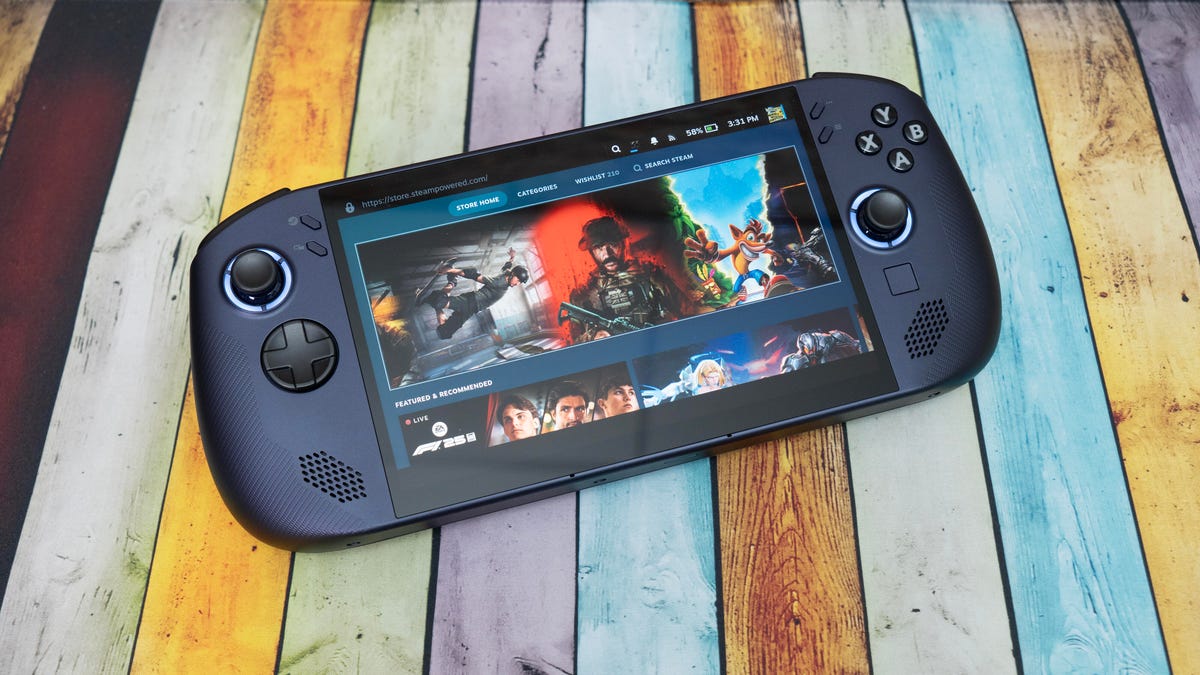 A black, rectangular handheld PC gaming device set against an abstract purple and orange background.