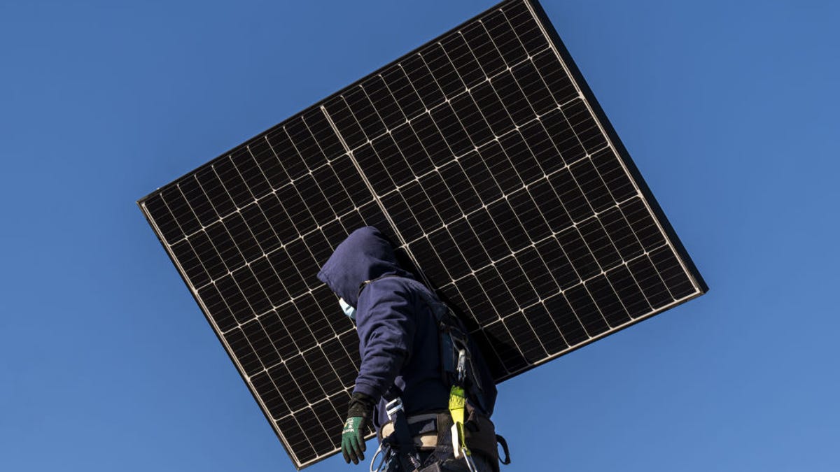 A solar panel installer carries a solar panel.