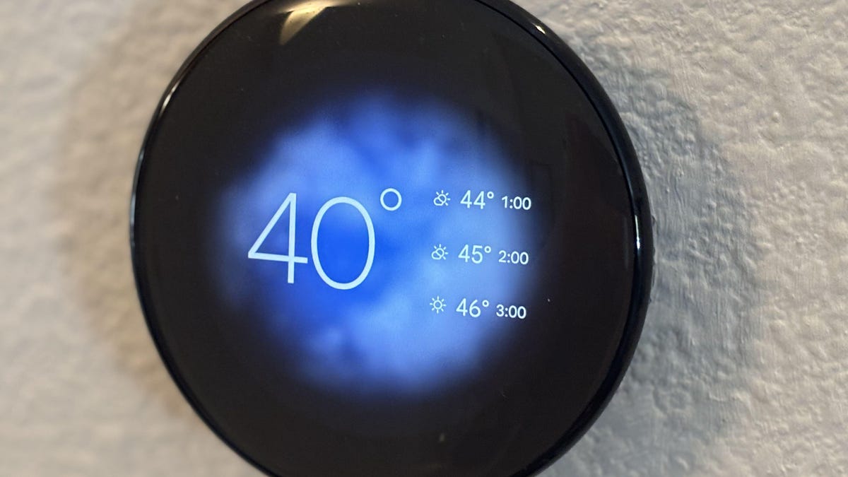 Nest Thermostat on wall showing temps and blue sky graphic.