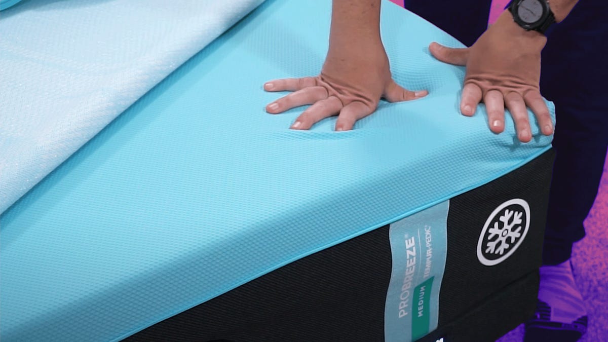 The Tempur-Pedic Pro Breeze mattress against a colorful background with a man's hands pushing down on the side of the bed.