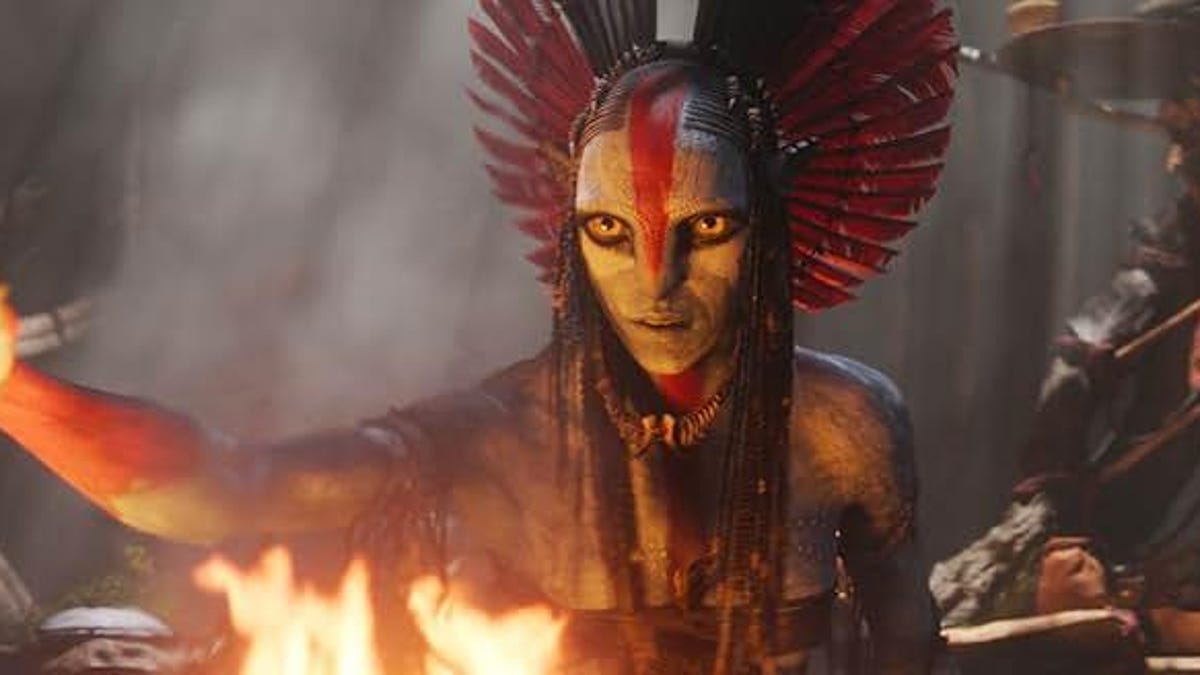 An alien Na'vi shaman stands in front of a flame.