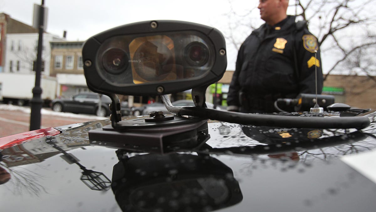 A police officer stands behind a cruiser that's mounted with an automated license plate reader.