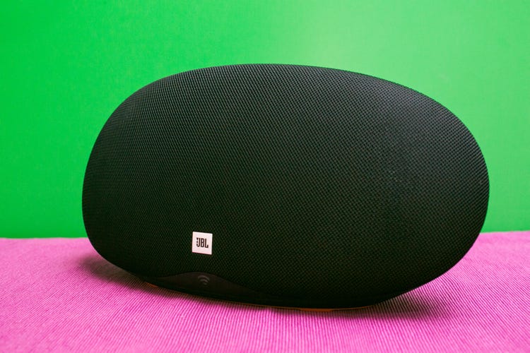 A black JBL Playlist Capsule speaker on a pink table against a green background.