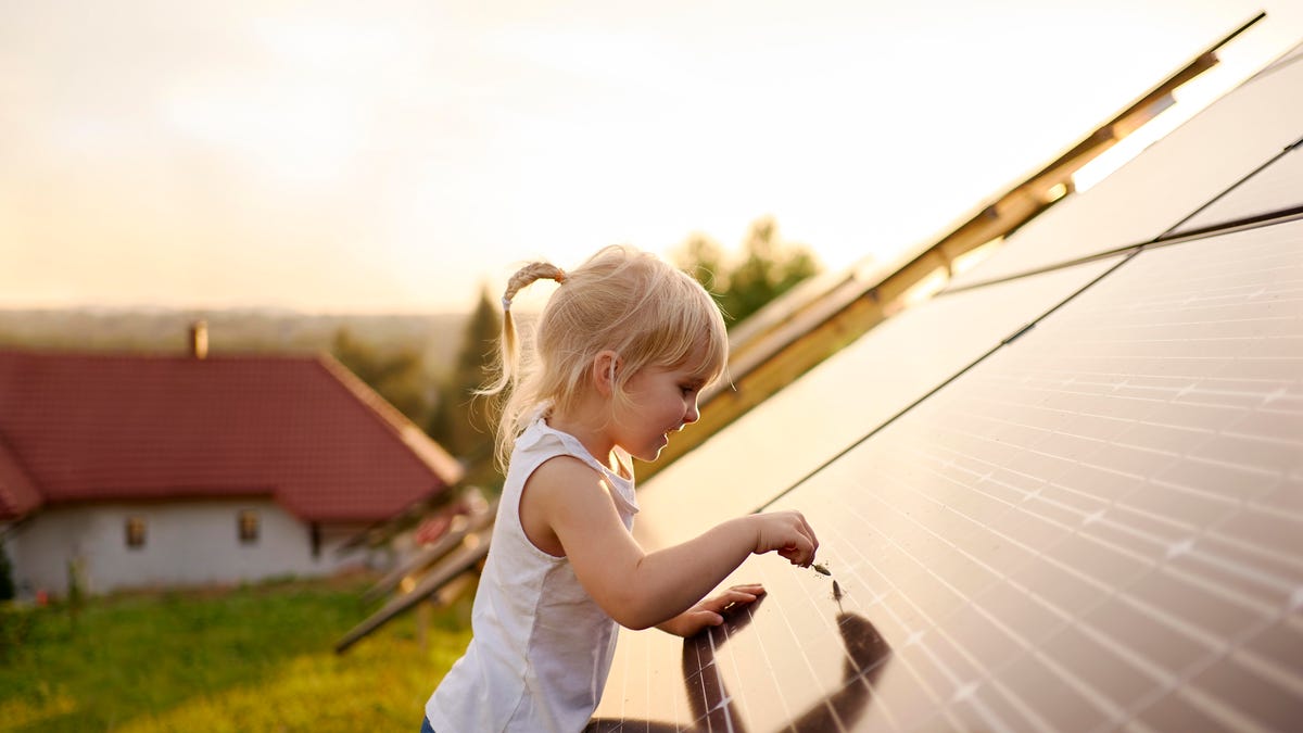 A little girl stands next to a solar panel, tracing her finger on it's surface