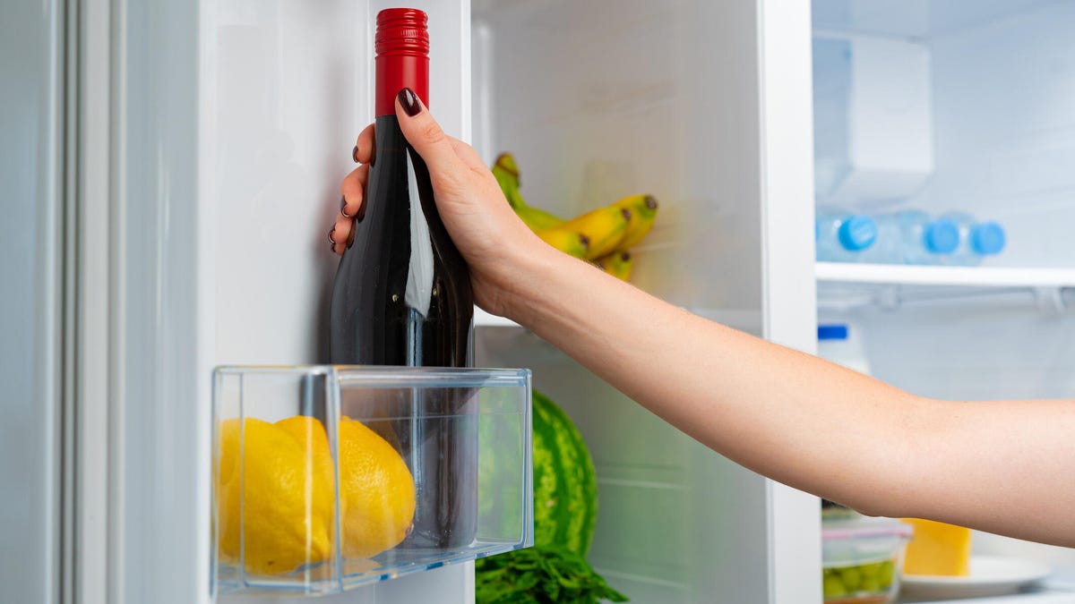 hand placing red wine bottle in fridge