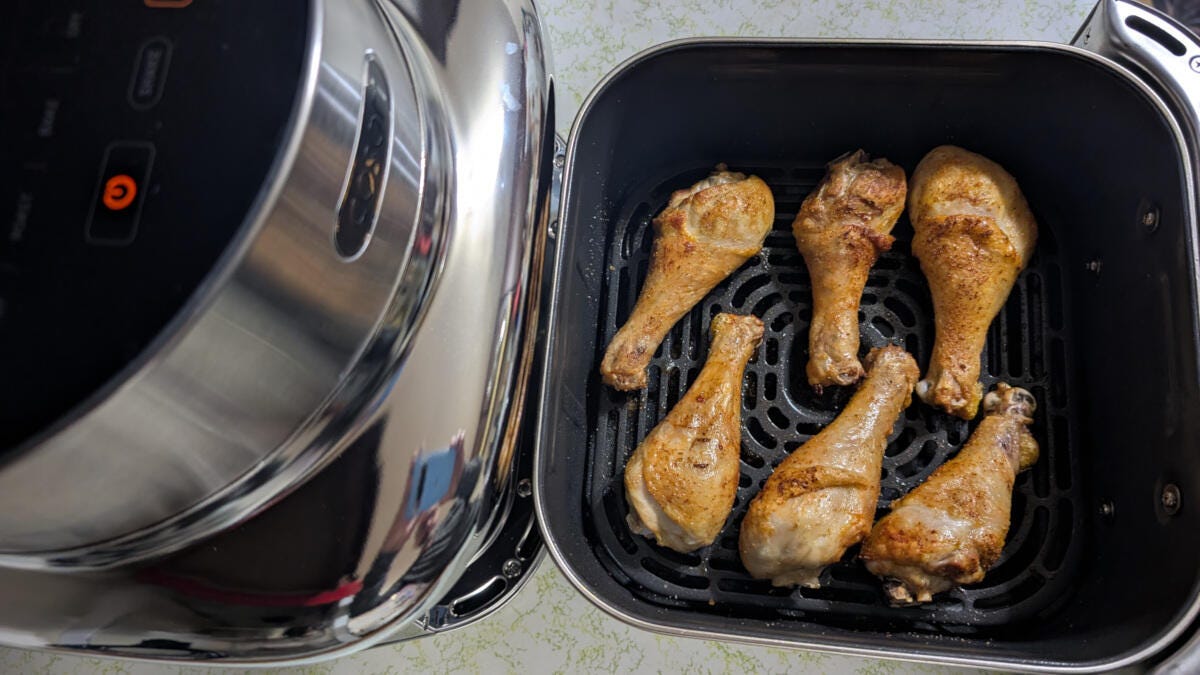 cosori-iconic-air-fryer-and-basket-resting-on-white-countertop-with-roasted-drumsticks
