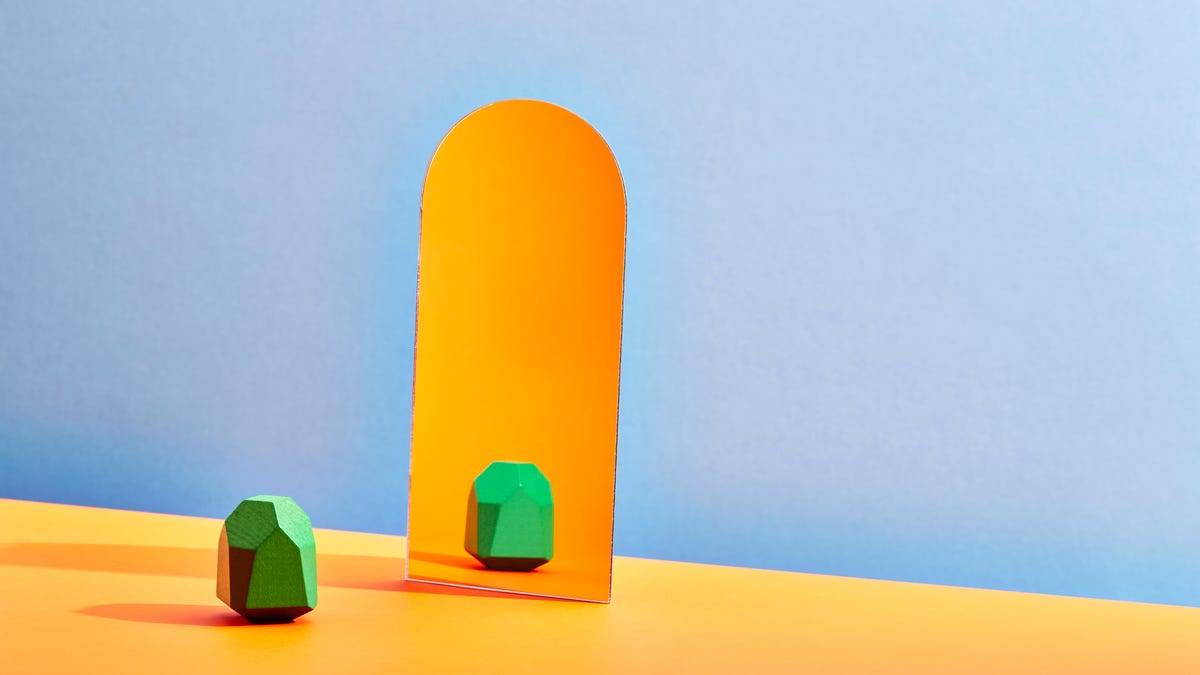 A green piece looking at another green piece in an orange mirror