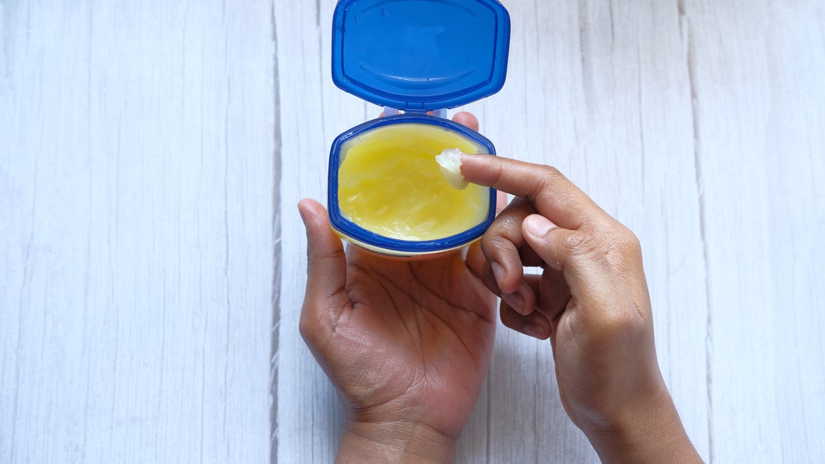 A finger scoops some vaseline out of a jar.