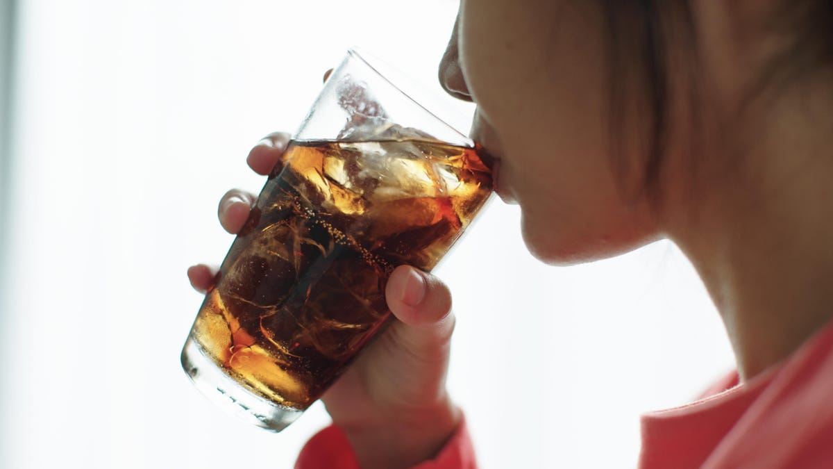 A close-up photo of a person drinking brown soda with bubbles out of a clear glass.