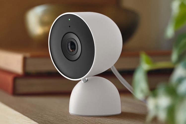 A wired Nest cam sits on a shelf by books.