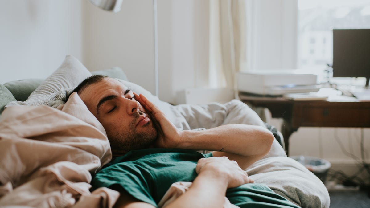 A man wakes up slowly, surrounded by bedding
