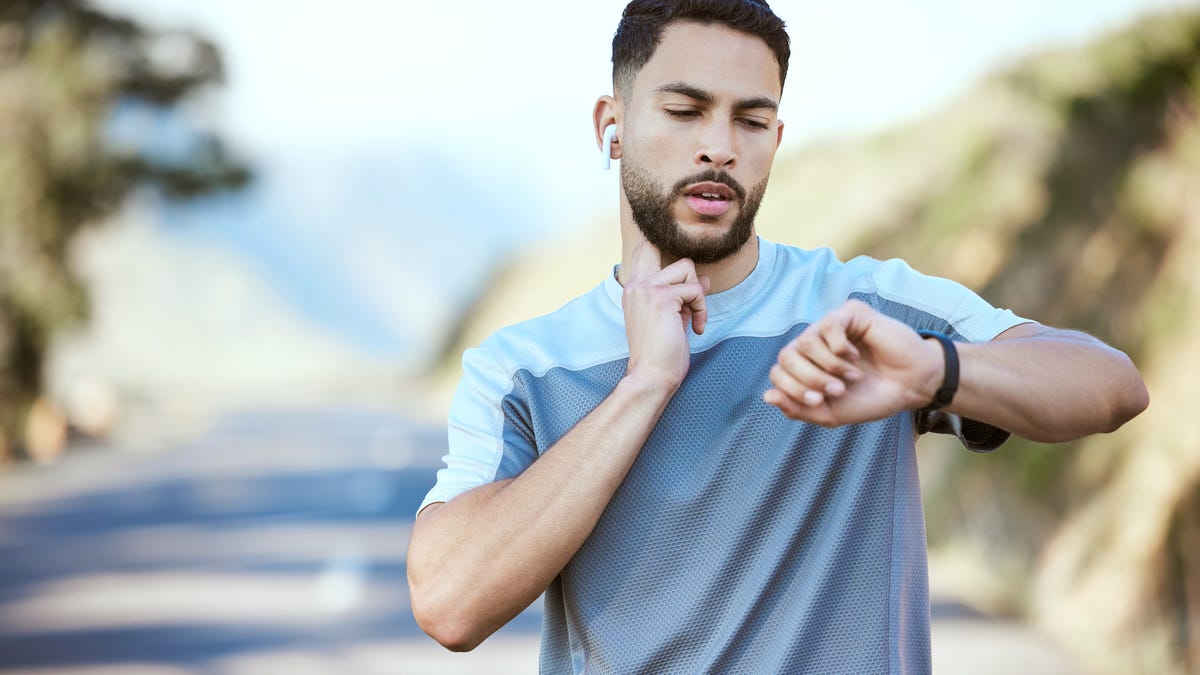 Runner checks their pulse on their neck, while also checking smartwatch.