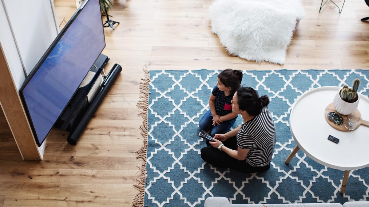 High angle view of mother and daughter watching television while sitting on floor at home